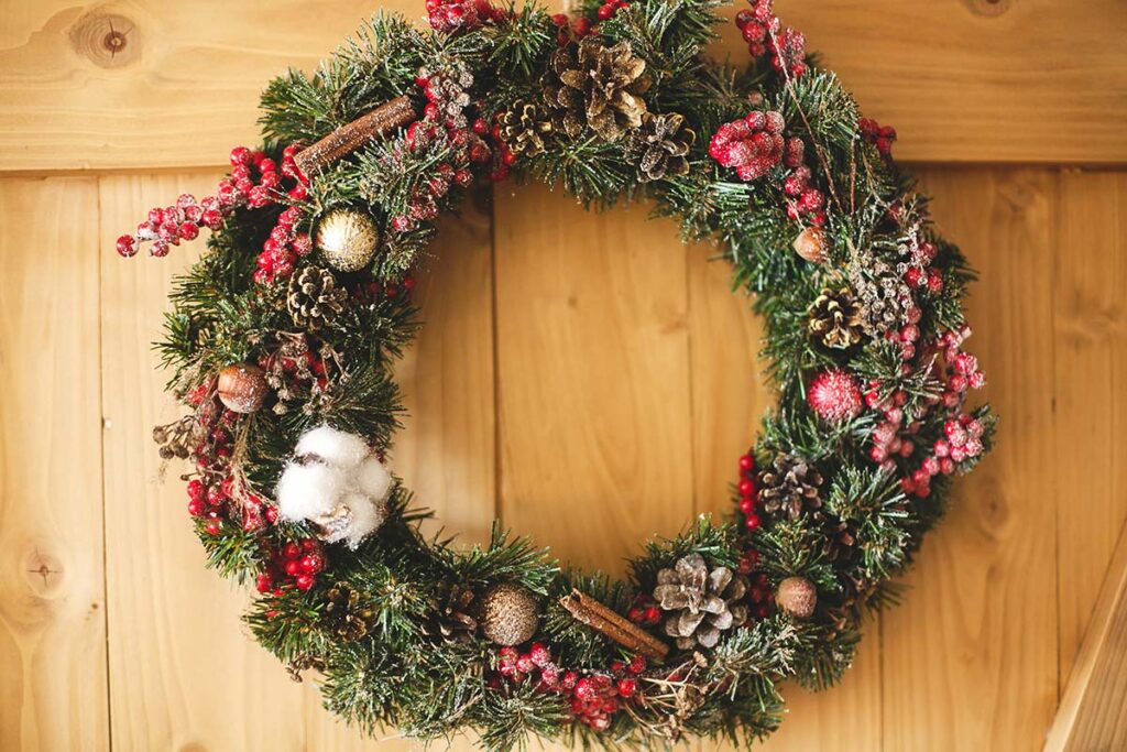 Christmas wreath hanging on rustic wooden door in house.Traditional christmas wreath with red berries and ornaments, pine cones and cinnamon on wooden background, holiday decor. Space for text
